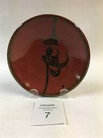 Front view of small round ceramic bowl showing copper red glaze and abstract tenmoku design inside.