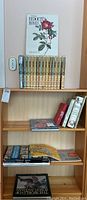Books arranged on two shelves showing gardening encyclopedias, Redoute's Roses botanical book, and various comic books.