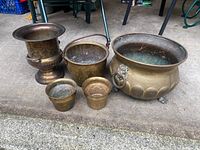 All five brass pots arranged on a concrete surface, showing comparative sizes and patina.
