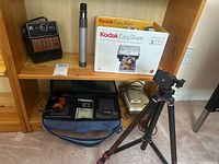 View of shelf with vintage camera, Kodak EasyShare printer dock in box, Citizen stereo, and tripod stand.