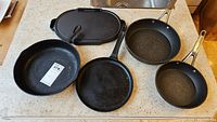Overview of all items including two cast iron frypans, one cast iron griddle, and two non-stick frying pans.