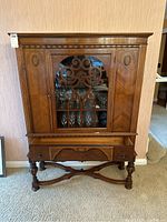 Front view of the wooden china cabinet showing glass fretwork door, drawer and turned legs