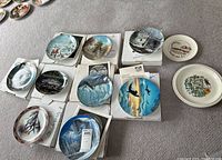 Multiple W.L. George fine china collector plates arranged on carpet with original boxes underneath each plate.