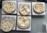 Five cream-tone bas-relief collector plates on top of boxes showing detailed figures, signed by Alberto SantAngela at the bottom edges.