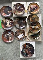 Top view of 11 Knowles Norman Rockwell collector plates arranged on carpet, some stacked on white boxes.