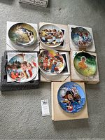 Seven Knowles collector plates arranged on floor alongside boxes. Plates feature nostalgic and whimsical scenes including children and nautical themes.