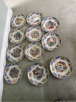 Twelve Jegou collector plates arranged on carpeted floor showing diverse artistic illustrations.