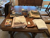 Lot of assorted dining table linens including tablecloths, placemats, napkins, and some furniture protection items like floor saver pads and felt pads, displayed on wooden dining table.