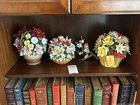 Shelf view with three porcelain floral baskets and porcelain bird figurine arranged in front of books