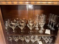 Top shelf with assorted glassware including coupe glasses, champagne flutes, and more with two tags visible showing item numbers 439 and 440.