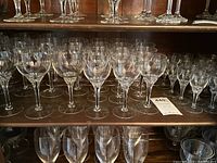 Shelves with multiple clear stemmed glasses including wine glasses and goblets.