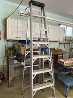 Full view of the 8 foot aluminum Featherlite step ladder in workshop setting, showing structure and steps.