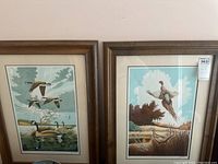 Two framed prints depicting birds - Canada geese and pheasants. Both signed by Lamy in 1977. Wooden frames and beige mats.