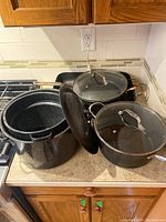 Set of enamel cookware including pasta cooker, soup pot, frying pan, and roasting pan on kitchen counter.