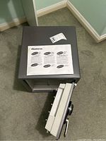 Top-down view showing the sealed user instructions on top of the closed safe and the safe door with combination lock detached and laying adjacent.