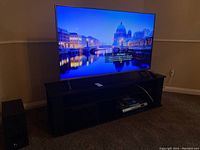 Front-left angle view of LG TV on black wooden stand, with Sony subwoofer at left and Shaw DVD player in right compartment