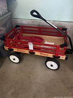 Full side view of the wooden Express Wagon showing red side panels, black handle with grip, white plastic wheels, and wooden bed.