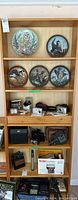 Front view of full wooden shelf with 6 compartments, showing decorative plates on upper shelves and vintage cameras on lower shelves for display only.