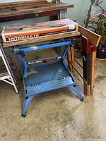 Black & Decker Workmate 400 workbench with wooden top, boxed Miter Mate accessory on top, and wooden sawhorse standing beside it