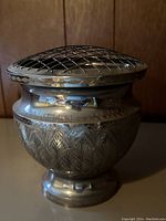Side view of the brass urn with decorative engravings and lattice lid.