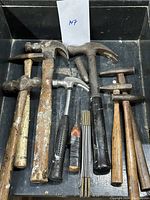 Top view of vintage hammers, mallets, and folding rulers in a black container showing wear, rust and patina.