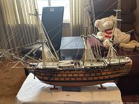 Side view of the large vintage plastic model ship on a white cloth-covered table showing the hull, rigging, and base stand labeled "Victory".