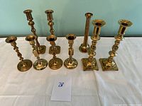 Front view of all seven brass candle holders showing variety in sizes and styles.
