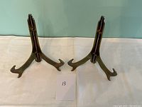 A pair of heavy brass plate stands side by side on a white cloth background, displayed upright showing shape and brass patina.