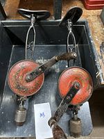 Top view of the pair of vintage hand crank drills showing red cracked paint, wooden handles, and metal gear mechanisms.