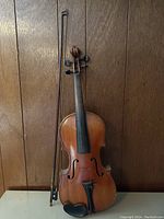 Front view of violin and bow upright against wood panel background
