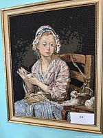 Framed needlepoint portrait of a woman knitting seated on a chair, detailed close-up of the entire artwork.
