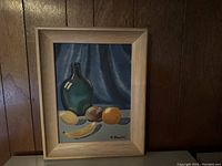 Framed oil on board still life painting showing green glass bottle and fruits including banana, lemon, apple, and orange, signed C. Smith.