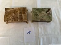 Pair of rectangular onyx jewelry boxes closed, one brown and one green, placed side by side on a white cloth.