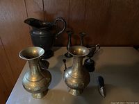 View of all items including dark silver pitcher, brass vases, candlesticks, small pitcher and a decorative item with handle.