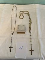 Overview photo showing two rosary necklaces laid out flat on white cloth next to a small box and a handwritten card with number 15.