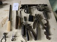Wide view of assorted hand tools on a white surface showing various types including files, pliers, clamps, and wire brush tool.