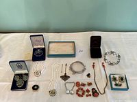 Full lot of vintage costume jewelry displayed on table, includes brooches, pearl necklaces, earrings, bracelet, and pins.