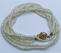Three strands of small genuine pearls twisted showing gold-tone floral clasp with pearl center.