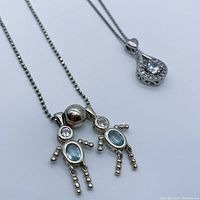Photo showing both sterling silver pendant necklaces; one with person-shaped pendant with blue and clear stones, another teardrop pendant with clear stones.