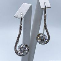 Pair of off-white moissanite dangling earrings on 925 sterling silver displayed on white earring stands showing front view.