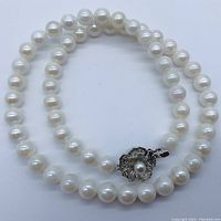 White round pearls strung in a loop with silver floral clasp visible
