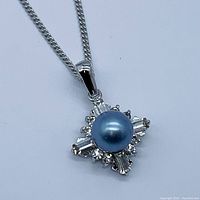 Close-up of pendant showing round blue pearl center and surrounding clear baguette and round stones