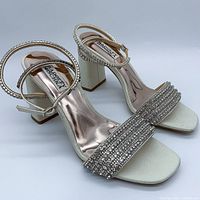 Pair of Badgley Mischka Becca crystal block heel sandals angled to display the side and heel details, showing the metallic crystals on the straps and the satin finish.