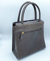 Side angle showing the brown ostrich leather handbag with two handles and visible textured leather pattern and gold zipper on side pocket.