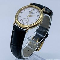 Side angle showing entire watch on stand with black leather strap and gold case.
