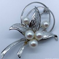 Front angled view showing the floral design, five round white Akoya pearls on silver leaves and stems with texture detail.