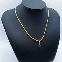 Full view of the gold plated pendant necklace displayed on a black bust showing the entire necklace and the pendant drop with green stone.