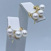 Front view of both earrings displayed on stands showing three pearls on curved gold-plated bar