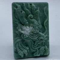 Front view of rectangular green jade pendant showing detailed carved dragon design in relief.
