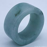 Wide band jade ring angled to show thickness and translucency, with slight natural inclusions visible.